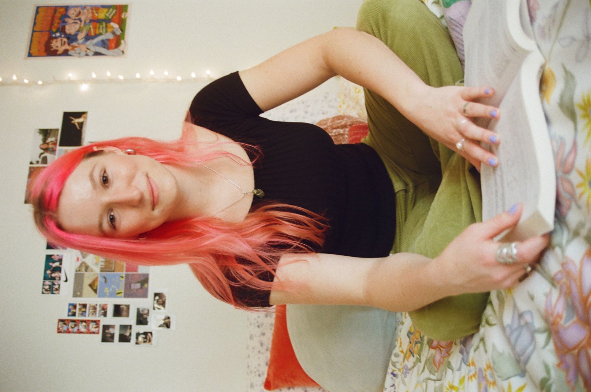 Grace, the person behind ChureThing, is sitting on a bed reading a book. She has pink hair and is wearing casual clothing.